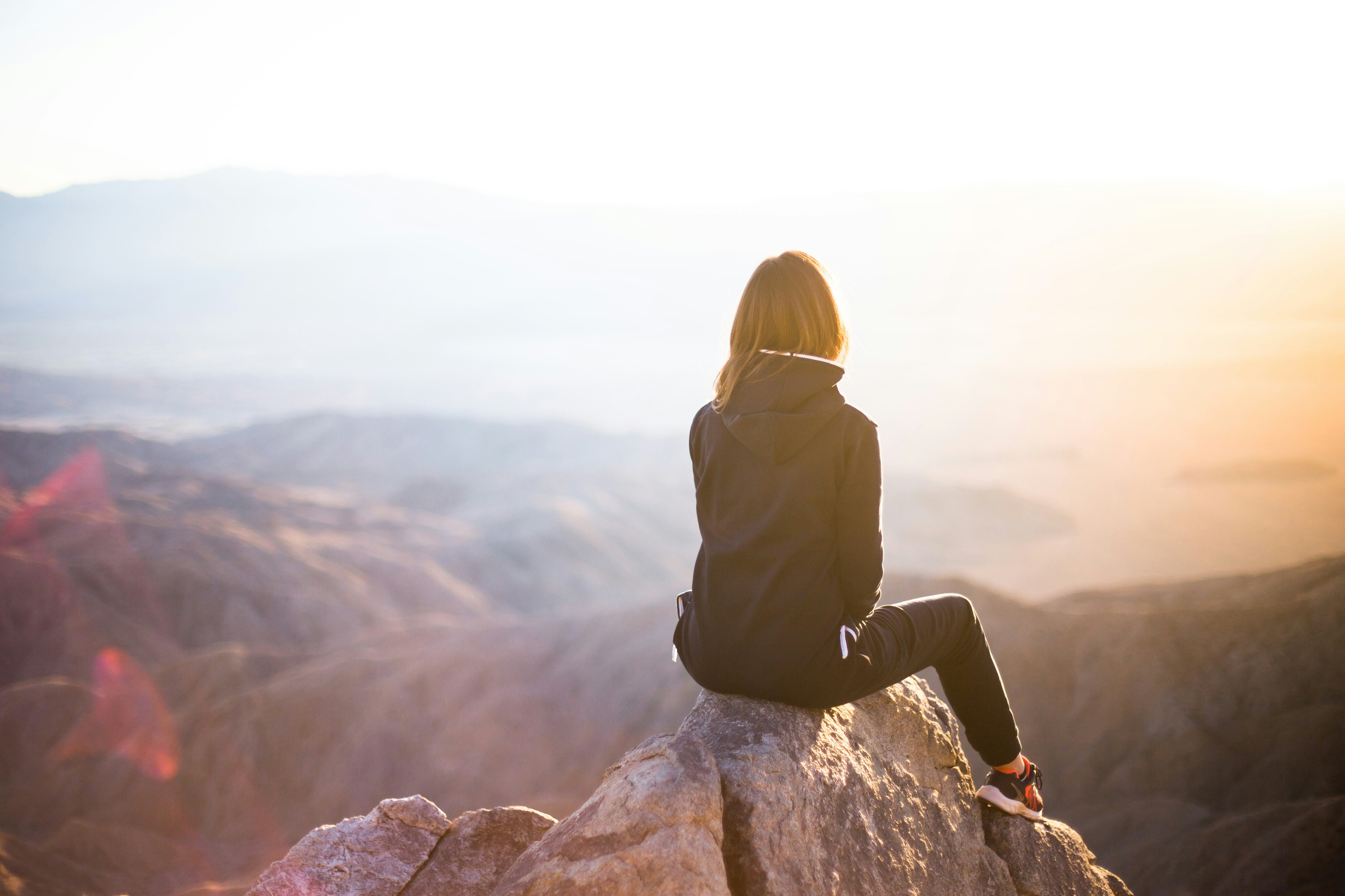 Person sitting on a mountain peak looking at the horizon